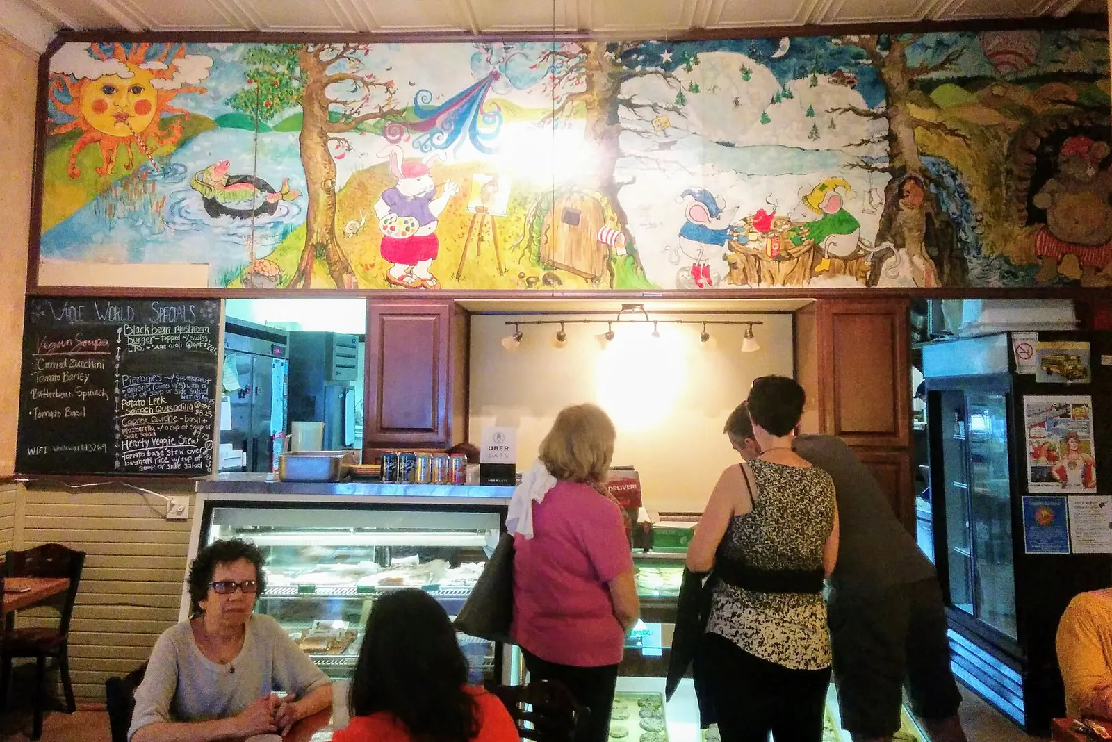 Customers at a counter under a painted mural, beside a chalkboard menu